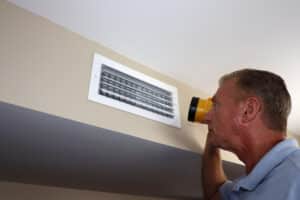 Man Inspecting a Home Rectangle Wall Air Vent with a Flashlight, HVAC Tune-Up.